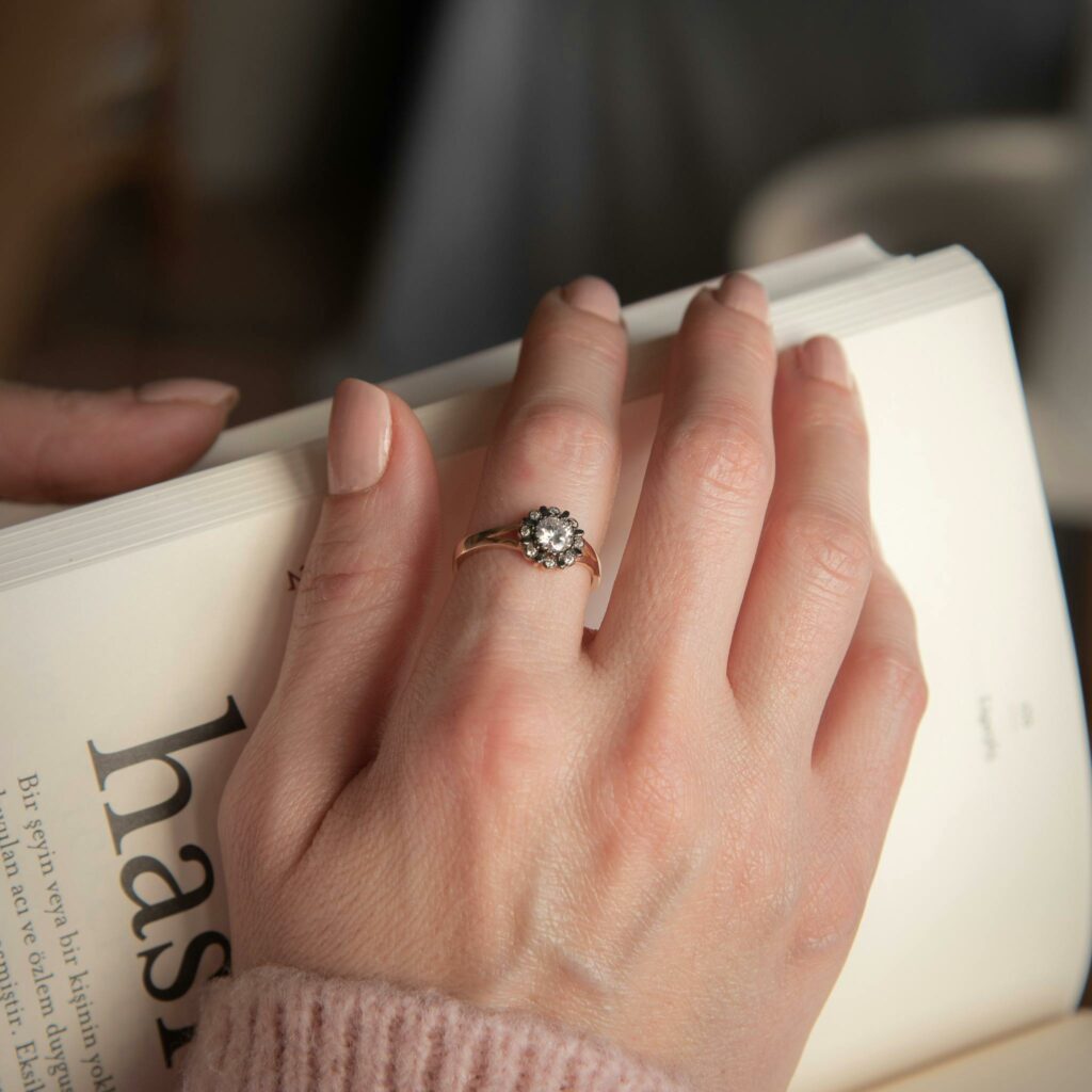 Close-up of a diamond ring on a hand holding an open book, showcasing chic elegance.